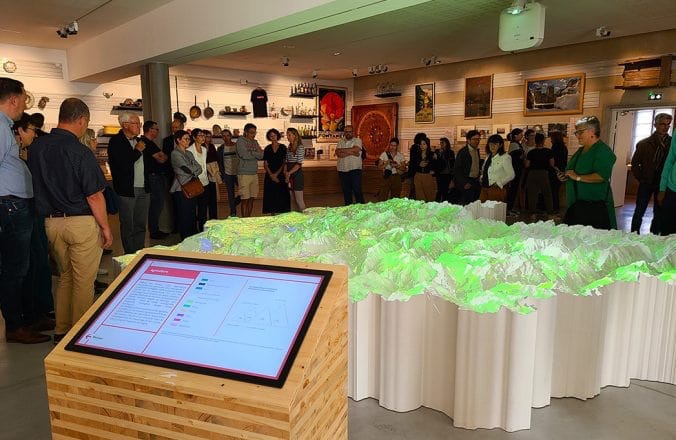 Maquette en relief avec projection interactive observée par de nombreux visiteurs.